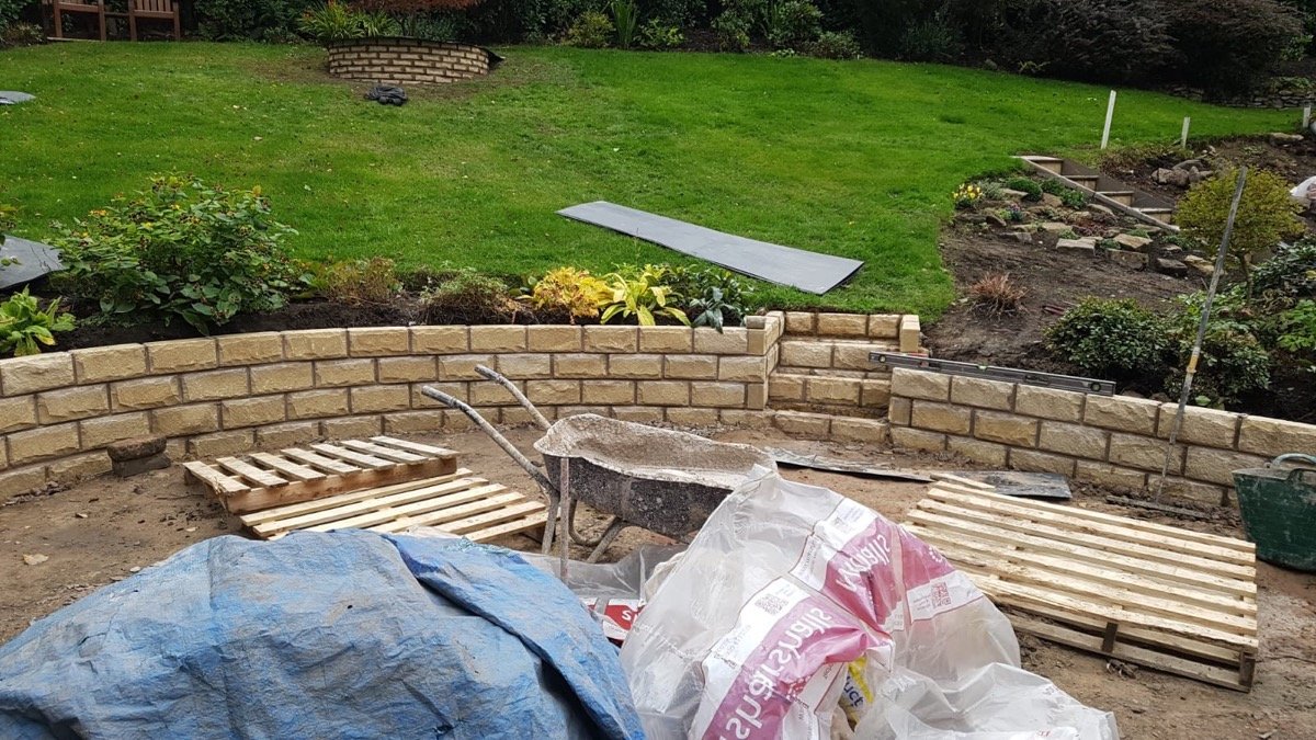 Curved sandstone-block retaining wall under construction in a large garden